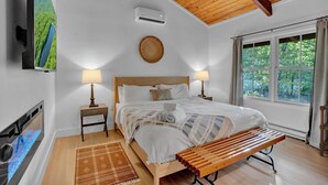 Une chambre à coucher avec un lit, des lampes de chevet, un banc en bois, une télévision et une fenêtre avec des rideaux.
