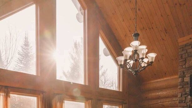 Interior acolhedor de cabana com lareira de pedra, sofás de couro e grandes janelas que permitem entrada de luz natural.