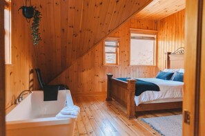 Ein Schlafzimmer einer Holzhütte mit Bett, Fenster, Holzstuhl und Badewanne.