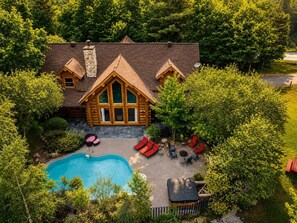A log cabin with a swimming pool, outdoor seating, and a stone chimney.