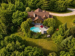 An aerial view of a house with a swimming pool, surrounded by dense trees. - Log Cabin: Heated Pool, Hot Tub & Volleyball (Mille-Isles)