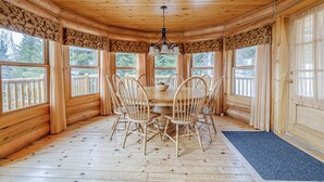 A wooden interior with a round table and chairs, large windows, and a wooden ceiling.