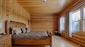 A log cabin bedroom with a wooden bed, a nightstand, and a window with curtains.