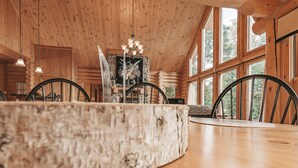 A rustic wooden interior with a large dining table, chairs, and a fireplace.