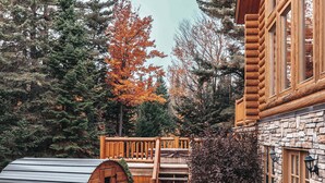 A log cabin with a stone exterior, a wooden deck, and a barrel.