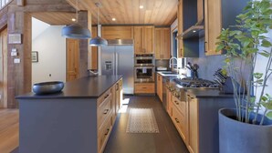 A modern kitchen with wooden cabinets, stainless steel appliances, and a central island. - Laurentian Chalet: 4K Cinema, Sauna & Hot Tub (Morin-Heights)
