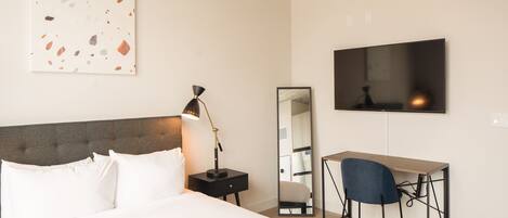 Een hotelkamer met een bed, bureau, stoel, bureaulamp, spiegel en televisie.