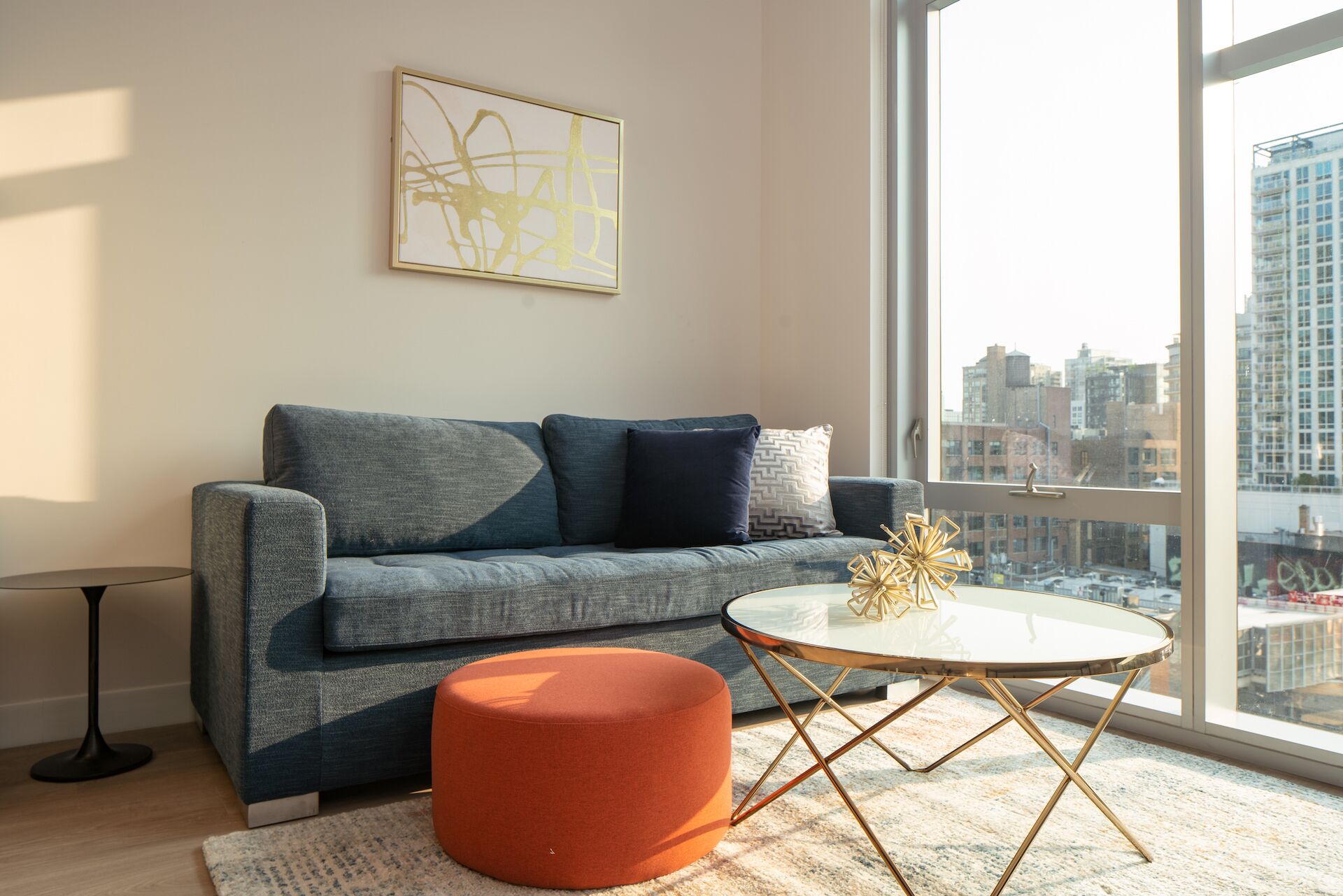 Un soggiorno moderno con un divano grigio, un tavolino rotondo e un poggiapiedi arancione. Un elemento decorativo dorato è posizionato sul tavolo.