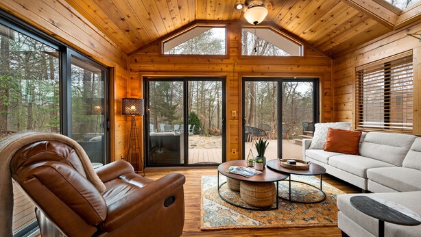 L’intérieur d’une cabane en rondins, avec un fauteuil inclinable en cuir, un canapé, une table basse et de grandes fenêtres donnant sur la forêt.
