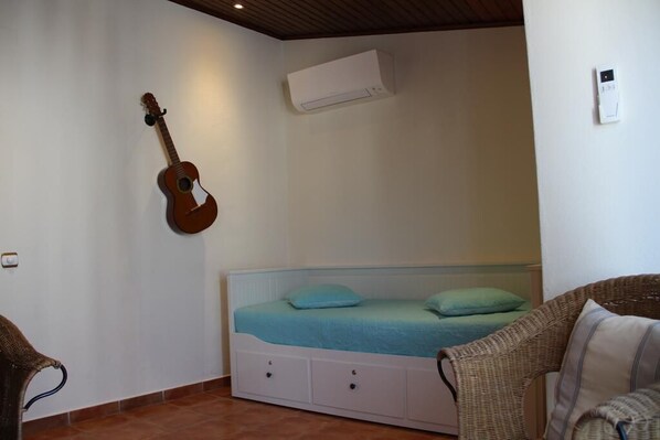 Une chambre avec un lit, une guitare, un climatiseur et une prise de courant au mur.
