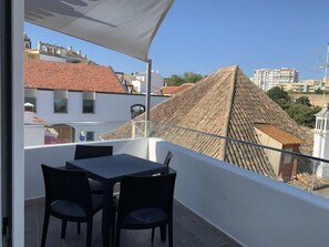 Un balcon avec une table et des chaises, donnant sur un paysage urbain avec des bâtiments et un ciel dégagé.