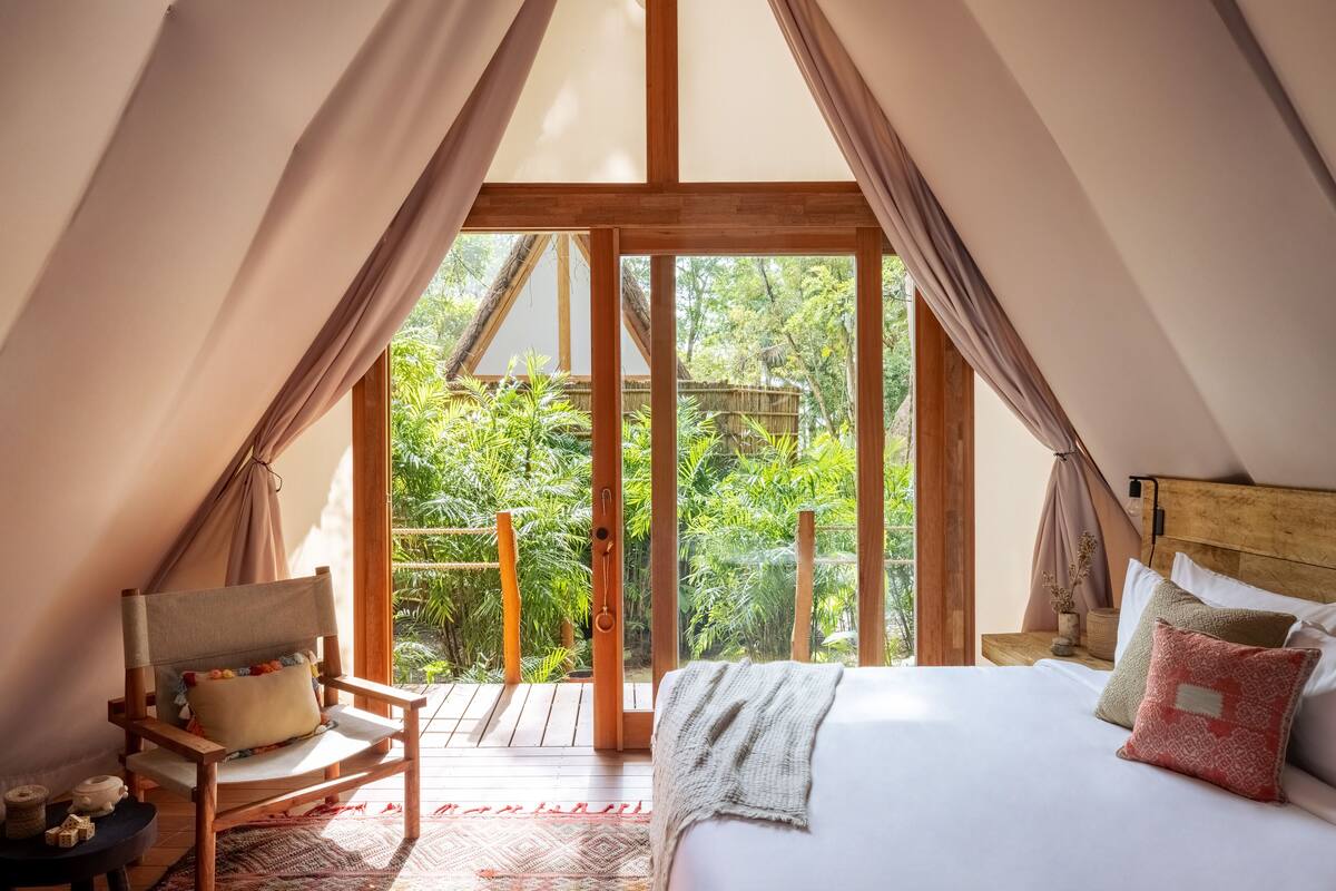 A cozy bedroom with a large bed, a chair, and a view of lush greenery outside.