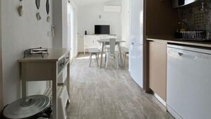 A modern kitchen with white cabinets, a dining area with a table and chairs, and a small side table with a kettle. - Friendly House (Lagos)