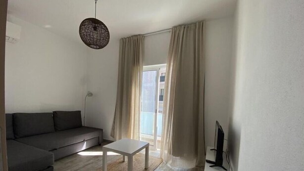 A modern living room with a grey sofa, a white coffee table, and a TV on a stand. - Friendly House (Lagos)