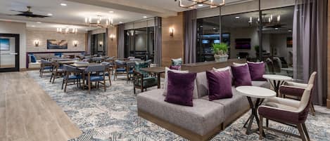 Een moderne hotellobby met een ruime zithoek, een bar en een eetruimte.