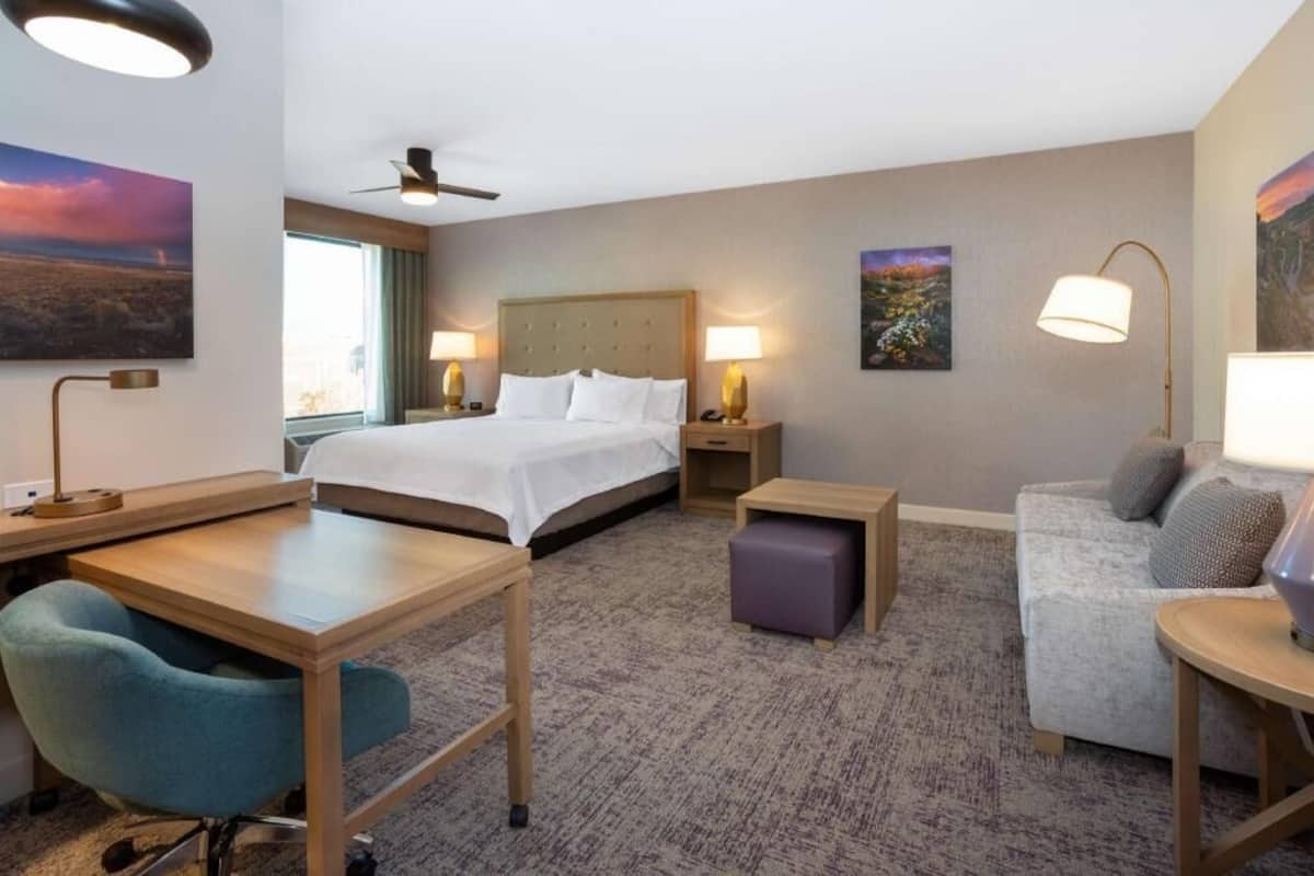 Ein Hotelzimmer mit Bett, Schreibtisch, Sessel, Sofa und Lampen.