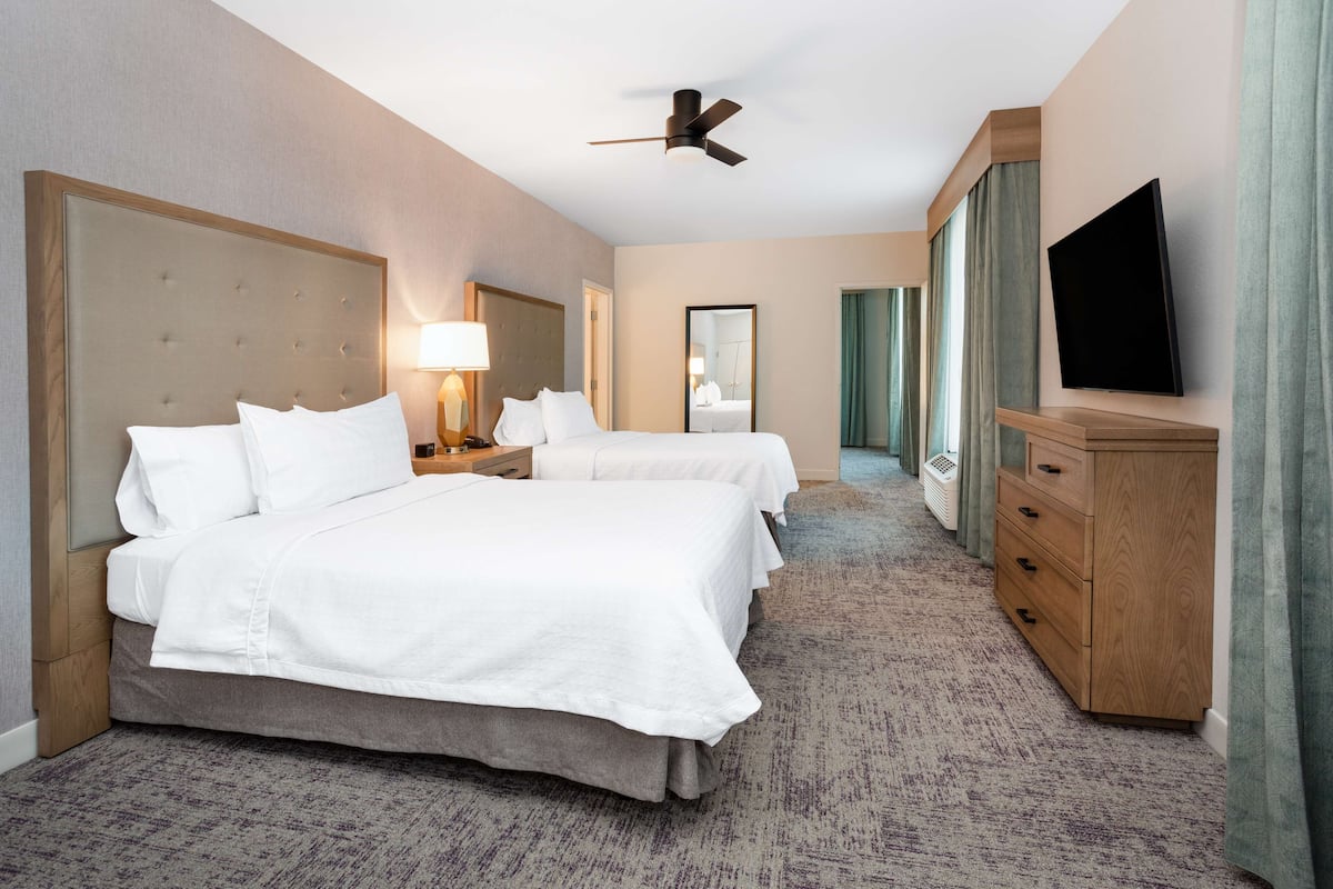 Ein Hotelzimmer mit zwei Betten, einem Deckenventilator, einem Fernseher und einer Holzkommode.