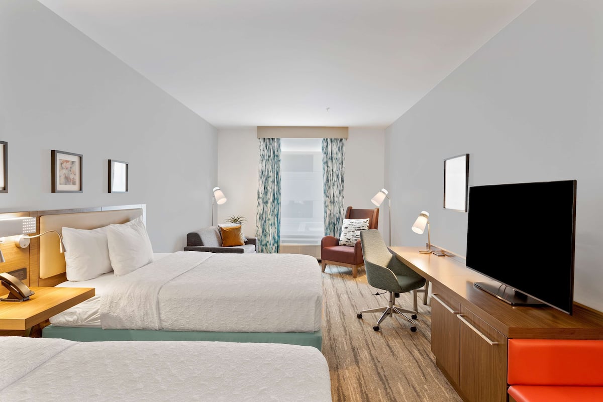 Habitación de hotel con dos camas, un escritorio, un televisor de pantalla plana, una silla y una lámpara de escritorio.