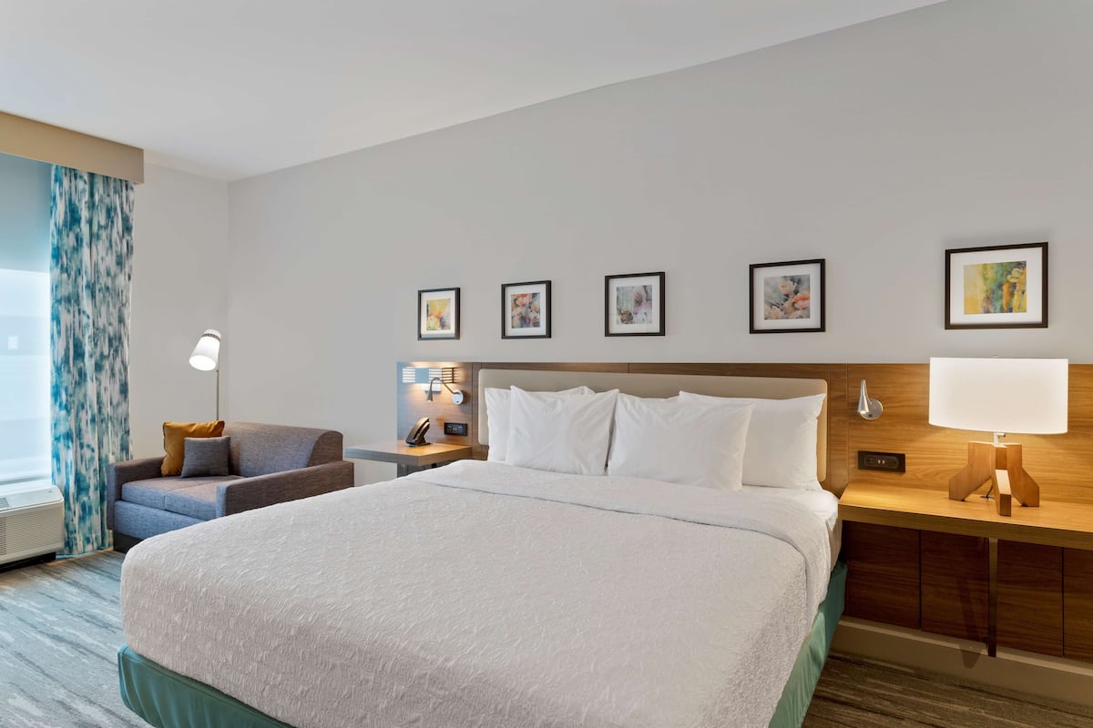 Una habitación de hotel con una cama grande, un escritorio con una lámpara, una silla y una ventana con cortinas.