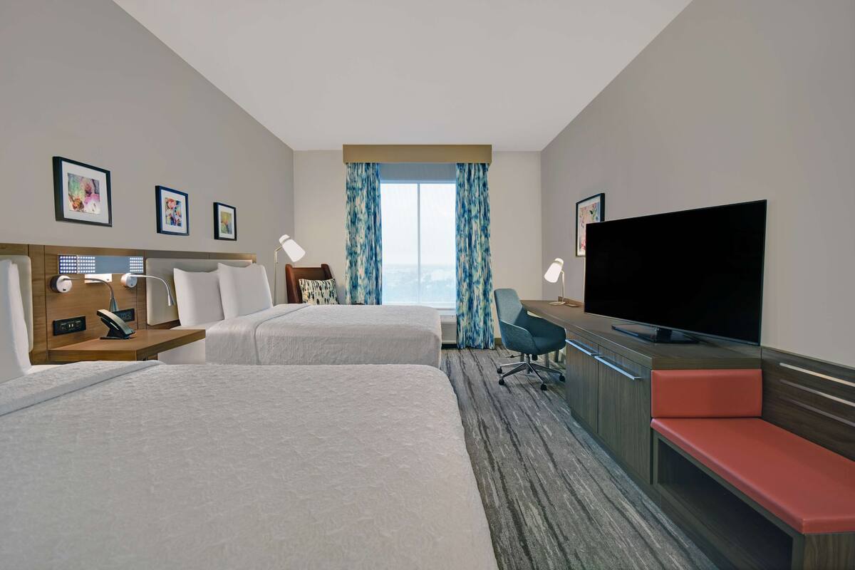 Habitación de hotel con dos camas, televisión, escritorio con silla y ventana con cortinas.