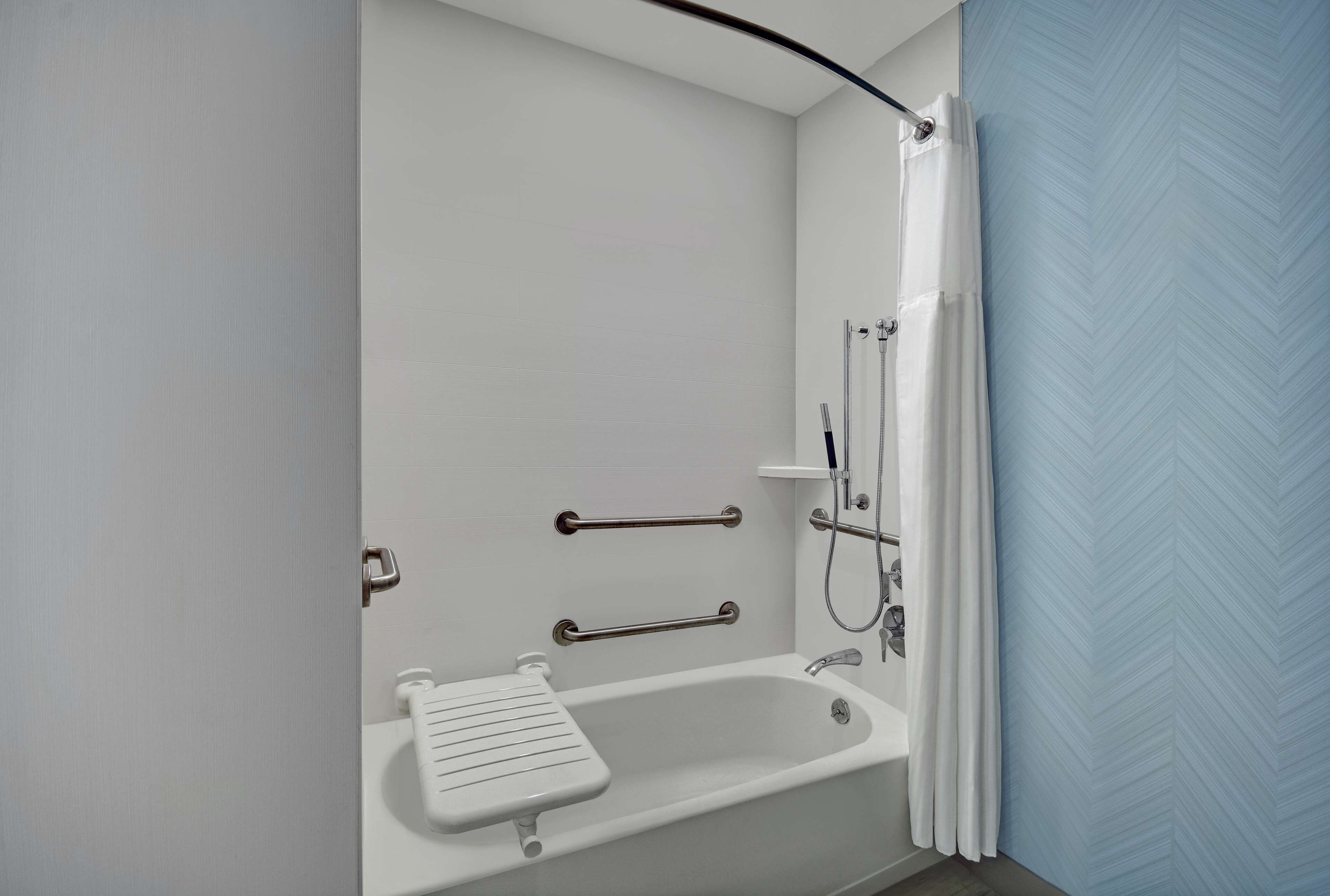 A bathroom with a bathtub, grab bars, a showerhead, and a white sink.