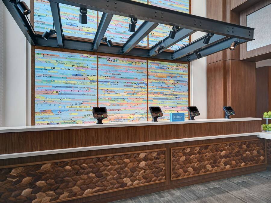 Un comptoir d’accueil d’hôtel avec un panneau décoratif en bois, un grand mur orné d’une carte et trois terminaux de paiement.