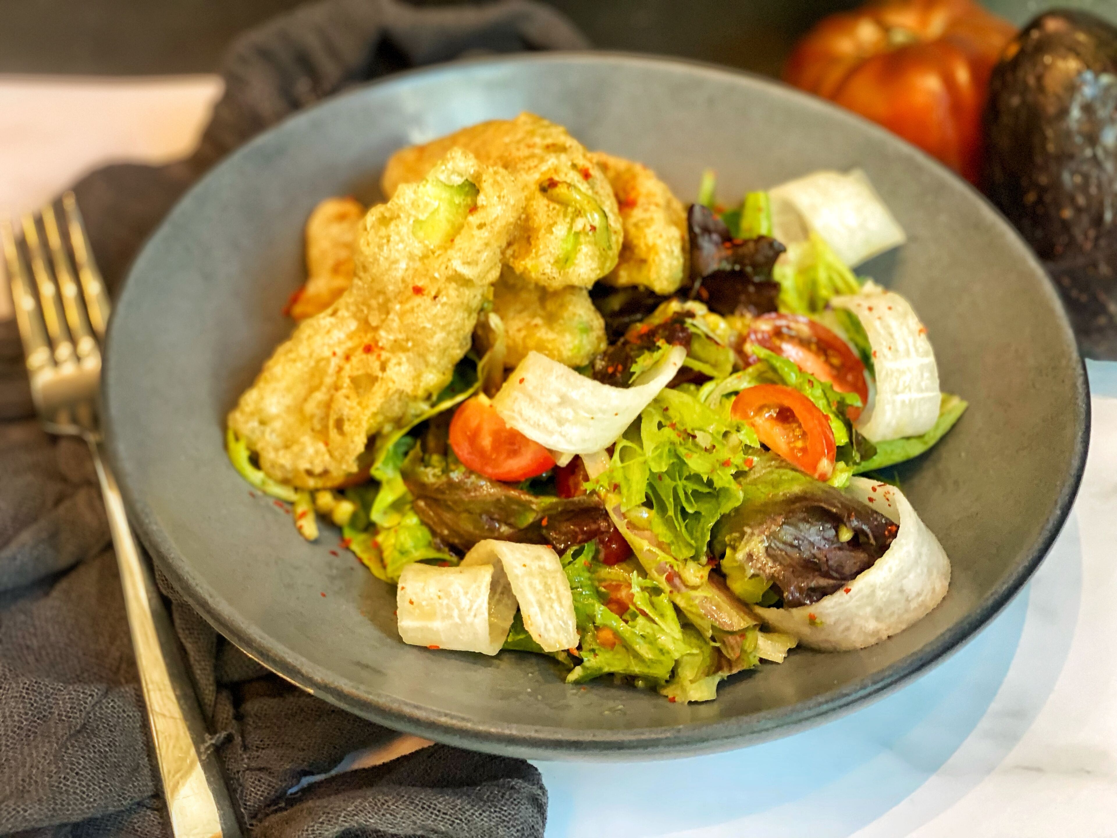 Ein Teller mit Salat, darunter Blattsalat, Tomaten und möglicherweise Fleisch, serviert auf einem dunklen Teller.