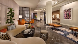 A modern hotel lobby with a sofa, chairs, a coffee table, and a large plant. - 106 Jefferson Huntsville, Curio Collection by Hilton (Huntsville)
