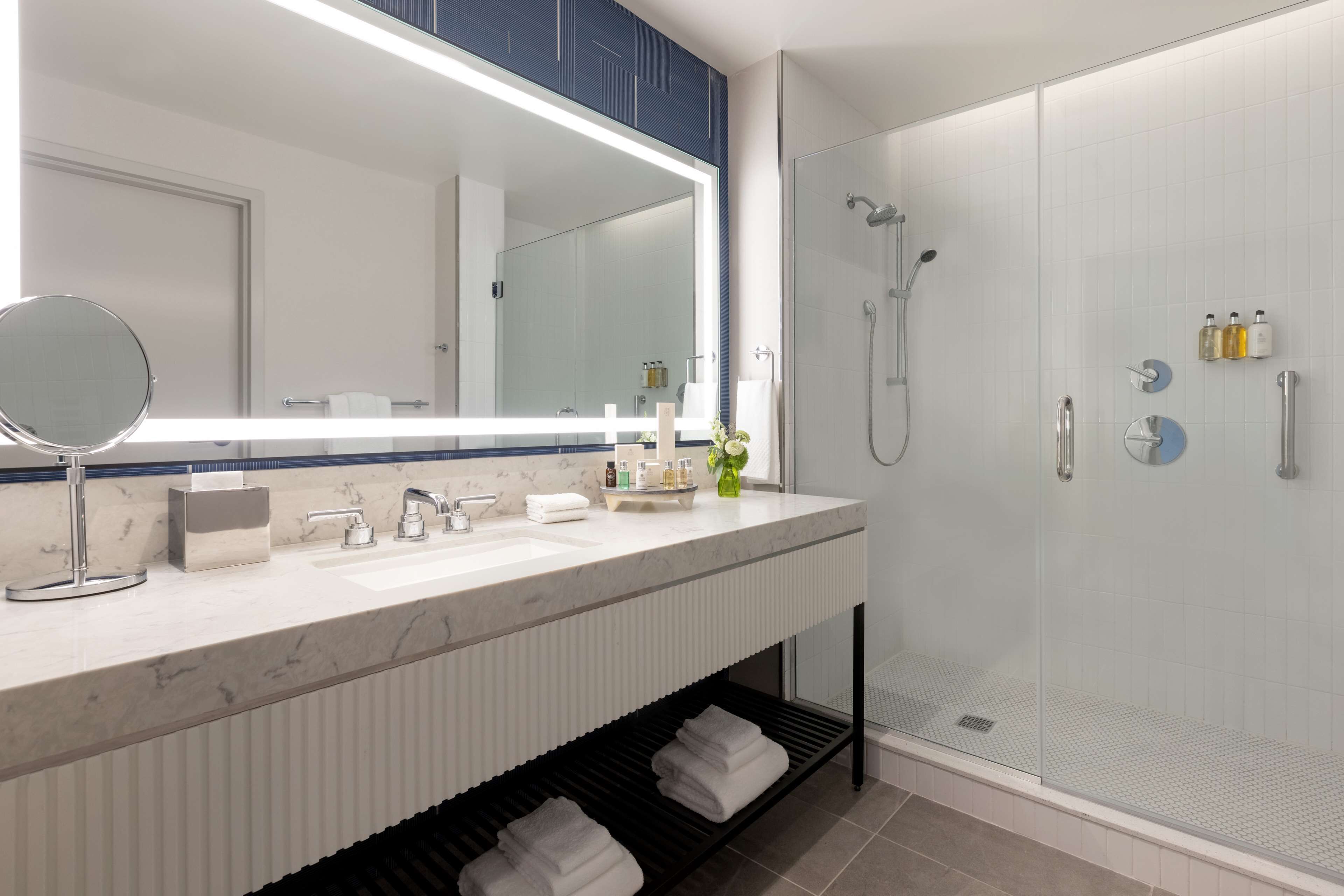 A modern bathroom with a large mirror, a shower with a glass door, and a vanity with a marble countertop.