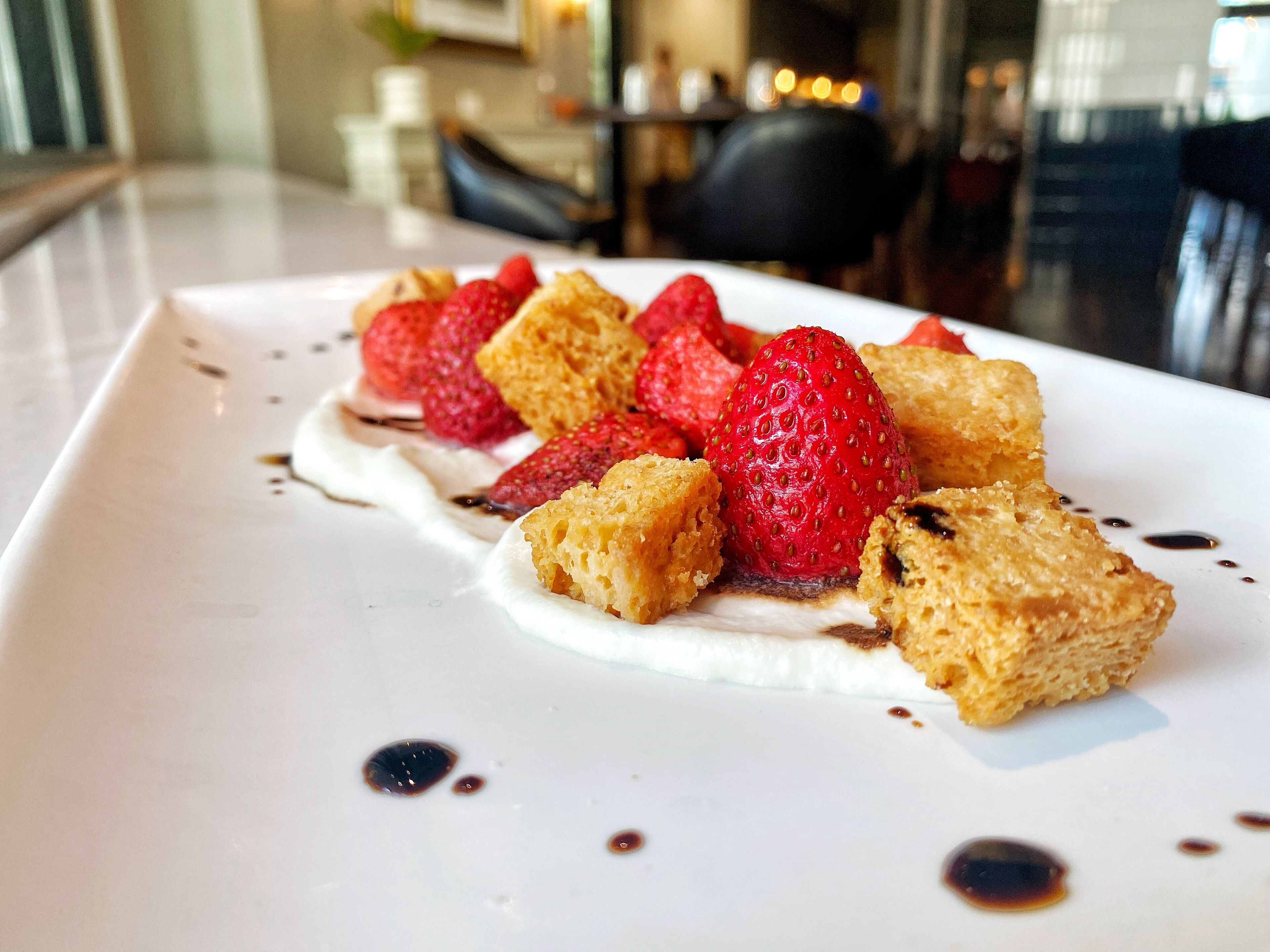 A dessert plate with strawberries and a creamy topping, served on a white plate with chocolate sauce.