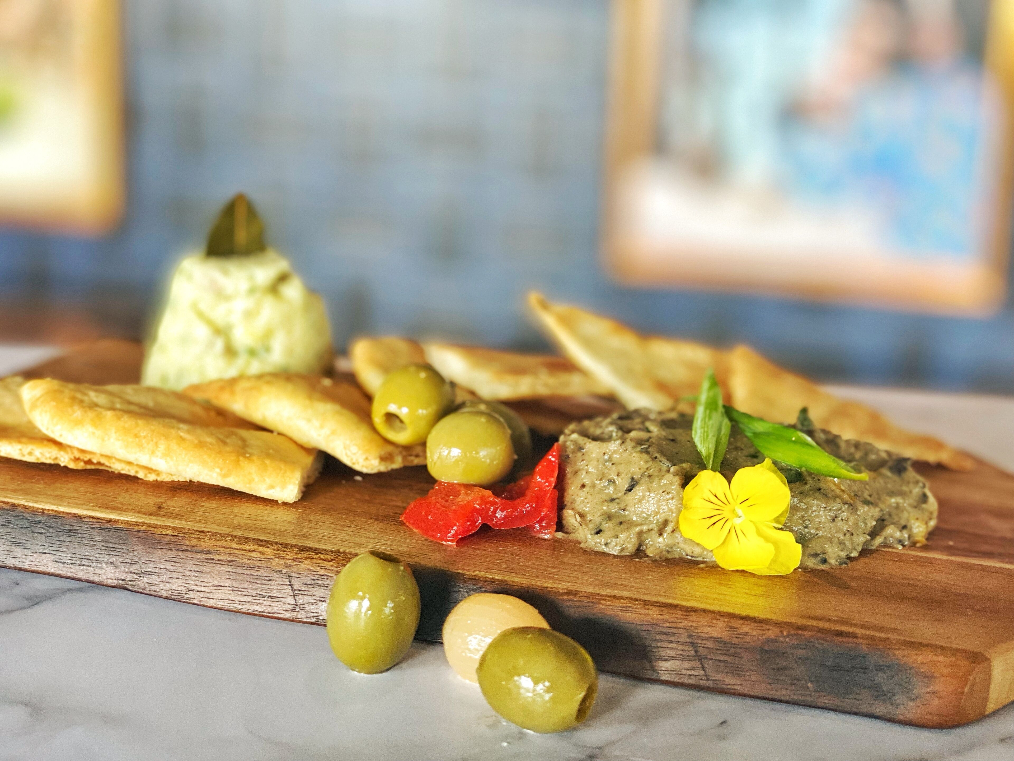 Una tabla de madera con diversos alimentos, como pan, aceitunas y un paté.