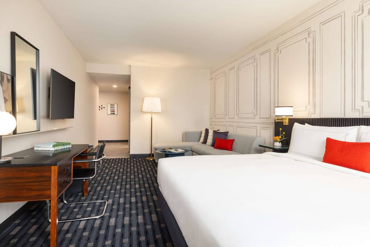 Een hotelkamer met een groot bed, een bureau met stoel, een bank, een televisie en een lamp.