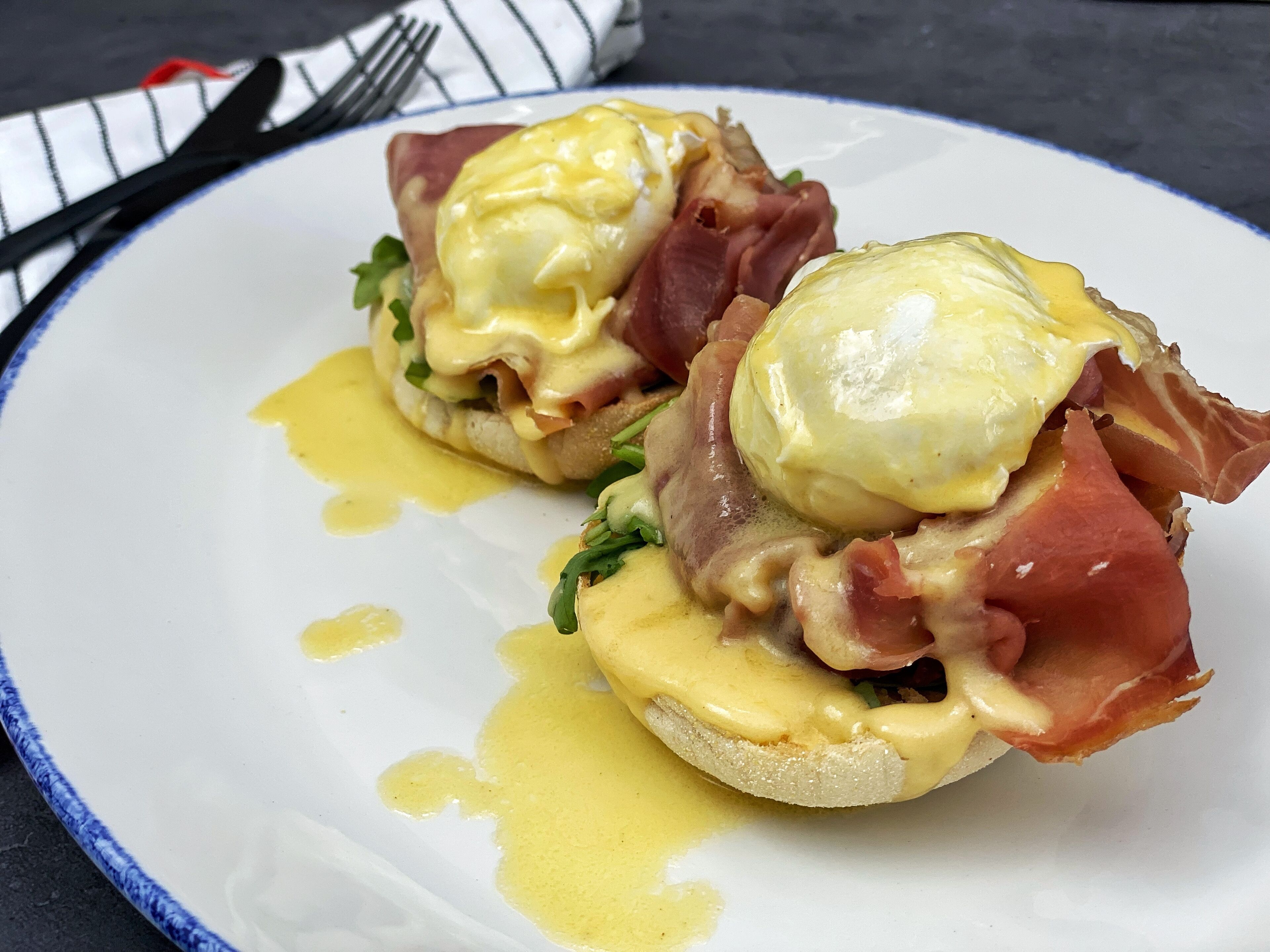 Ein Teller mit zwei Eggs Benedict Sandwiches, belegt mit Schinken und Hollandaise-Soße.