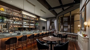 A bar area with a long counter, multiple stools, and a variety of bottles and glasses. - 106 Jefferson Huntsville, Curio Collection by Hilton (Huntsville)
