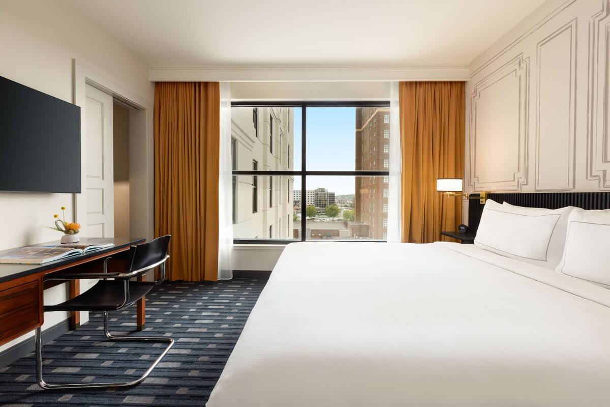 Hotelkamer met groot bed, bureau met stoel, flatscreen televisie en raam met gordijnen.