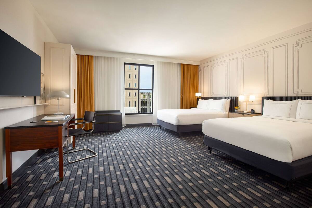 Hotelkamer met twee bedden, een bureau, een stoel, een televisie en een raam met gordijnen.