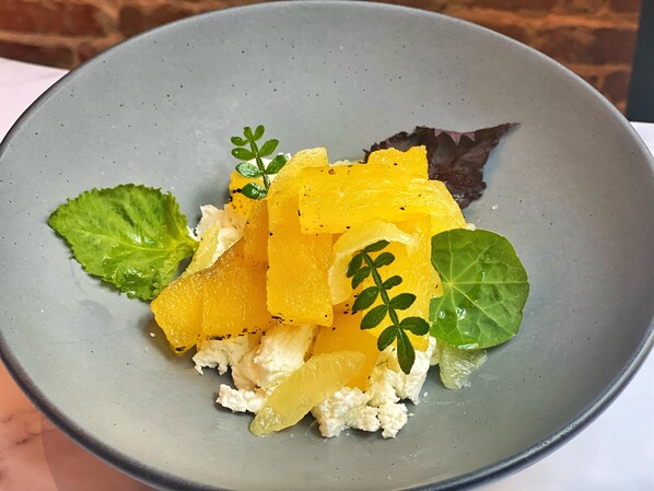A plate with a dish consisting of yellow fruit, white cheese, and green leaves. - 106 Jefferson Huntsville, Curio Collection by Hilton (Huntsville)