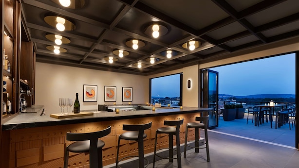 A modern kitchen with a bar area, bar stools, and a large window overlooking a cityscape. - 106 Jefferson Huntsville, Curio Collection by Hilton (Huntsville)