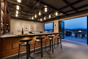 Una cocina moderna con barra, taburetes y un amplio ventanal con vistas a un paisaje urbano.