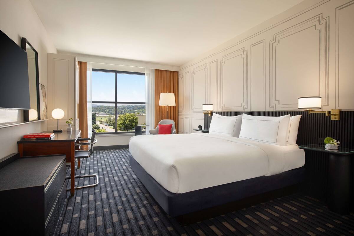Een hotelkamer met een groot bed, een bureau met stoel, een televisie en een raam met uitzicht op de stad.