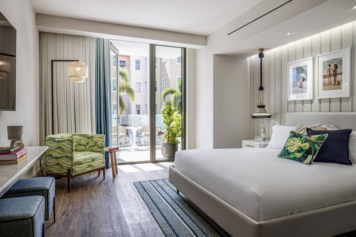 Ett modernt hotellrum med en stor säng, ett skrivbord, en stol och en balkong med utsikt över staden.