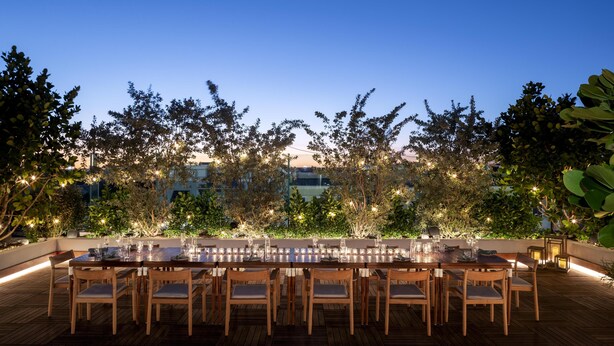 An outdoor dining area with a long table and chairs, surrounded by greenery and string lights. - The Ray Hotel Delray Beach, Curio Collection by Hilton (Delray Beach)