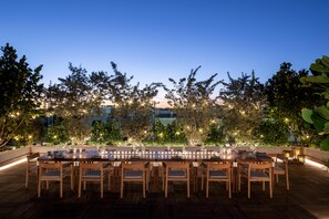 An outdoor dining area with a long table and chairs, surrounded by greenery and string lights. - The Ray Hotel Delray Beach, Curio Collection by Hilton (Delray Beach)