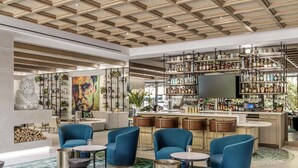 A modern bar area with blue seating, a large TV, and a variety of bottles. - The Ray Hotel Delray Beach, Curio Collection by Hilton (Delray Beach)