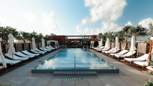 A pool area with lounge chairs and umbrellas, a clear sky, and a wooden deck. - The Ray Hotel Delray Beach, Curio Collection by Hilton (Delray Beach)