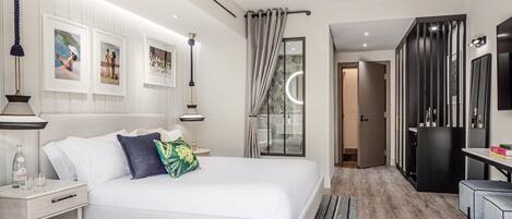 A modern hotel room with a large bed, a bedside table, a desk, and a wardrobe.