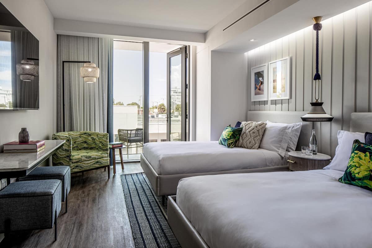 Ett modernt hotellrum med två sängar, en matplats och en balkong med utsikt.