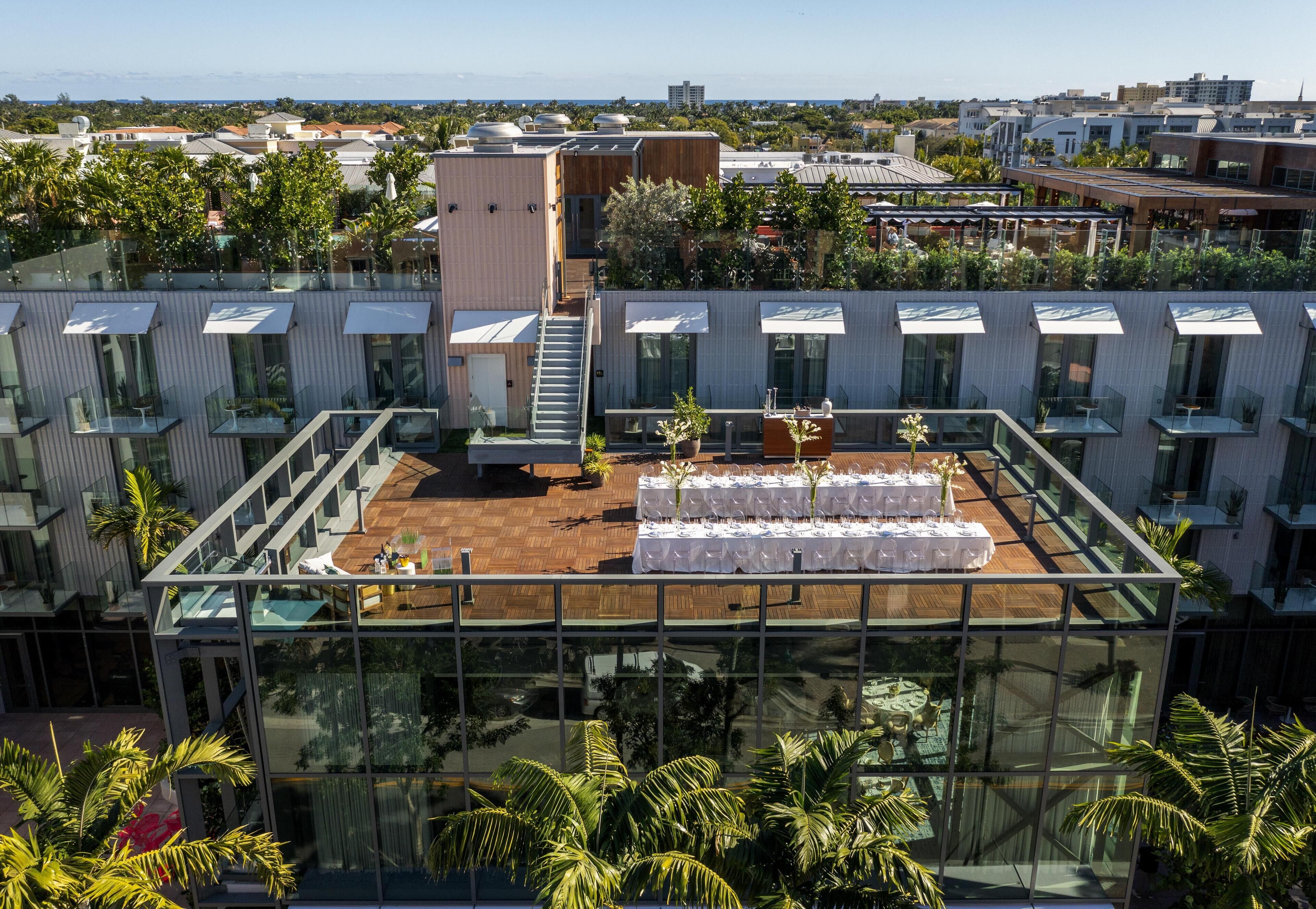 Una terraza moderna en la azotea con barandas de vidrio, un área de comedor preparada para un evento pequeño y vistas del paisaje urbano circundante.