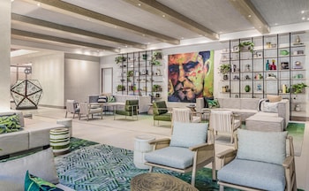A modern bar area with blue seating, a large TV, and a variety of bottles. at The Ray Hotel Delray Beach, Curio Collection by Hilton