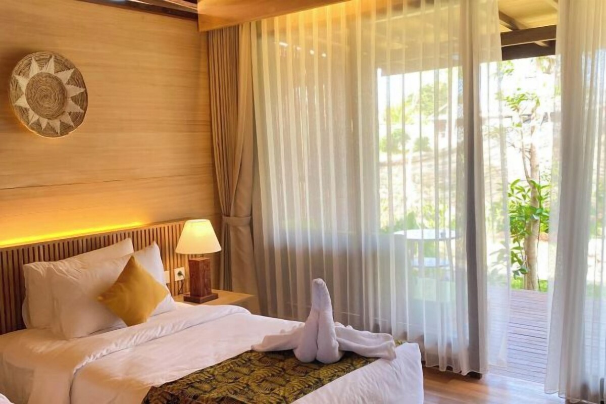 Une chambre d’hôtel avec un lit, une table de chevet, une lampe et des rideaux légers.
